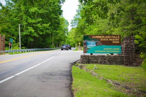 Sign for Cumberland Falls State Resort Park with a car approaching on a tree-lined road.