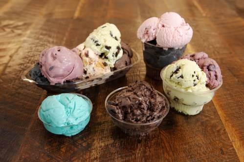A variety of ice cream scoops in bowls, including mint, chocolate, and berry flavors, on a wooden table.