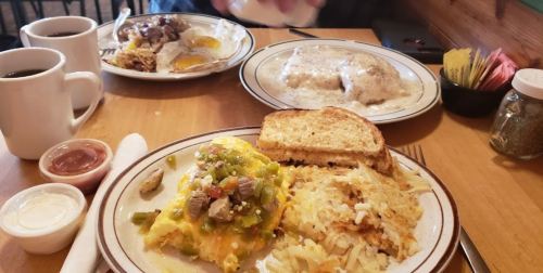 A table with two plates of breakfast: one with an omelet, hash browns, and toast; the other with biscuits and gravy.