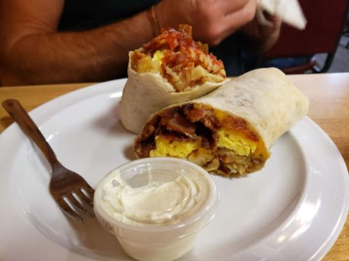 A plate with two breakfast burritos and a small cup of sour cream, with a fork beside it.