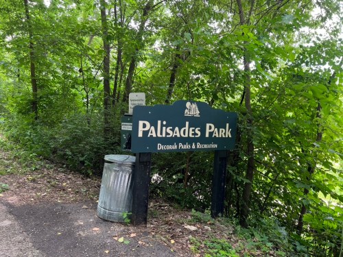 Sign for Palisades Park surrounded by greenery, with a trash can nearby.