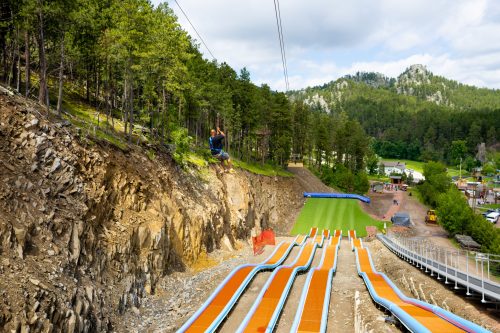 A person zip-lining over a hillside with colorful water slides and trees in the background.