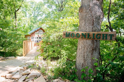 A wooden sign reading "Moonlight" next to a path leading to a small cabin surrounded by lush greenery.