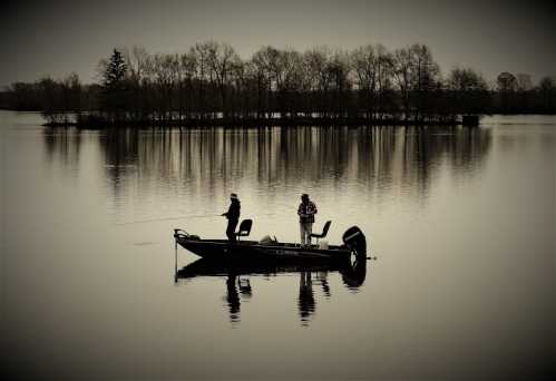 Two fishermen in a boat on a calm lake, surrounded by trees, with a muted, reflective atmosphere.