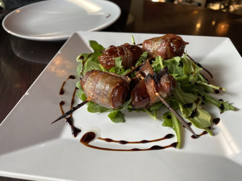 A plate of skewered, wrapped meat on a bed of arugula, drizzled with balsamic reduction.