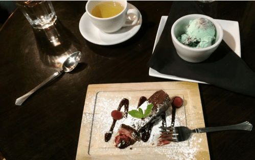 A dessert plate with chocolate cake, raspberries, and mint, alongside a cup of tea and a scoop of mint ice cream.