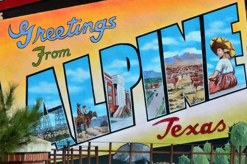 Colorful mural reading "Greetings From Alpine, Texas," featuring a woman in a sombrero and scenic landscapes.
