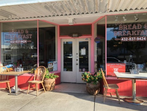 Exterior of a cozy café named "Bread & Breakfast," featuring pink accents and outdoor seating.