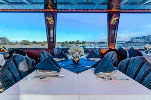 Elegant dining setup with blue napkins and a floral centerpiece, overlooking a scenic waterfront view.