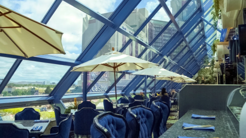 A modern restaurant with blue decor, large windows, and outdoor umbrellas, offering a view of the city skyline.