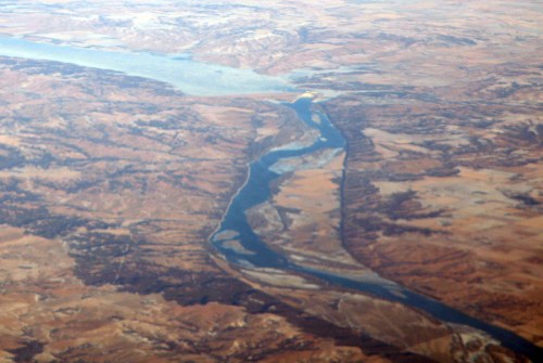 Aerial view of a winding river cutting through arid, mountainous terrain with sparse vegetation.