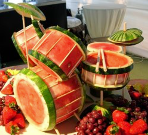 A creative display of watermelon drums surrounded by strawberries and grapes, featuring mini umbrellas as decorations.