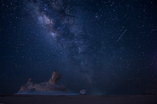 A starry night sky filled with the Milky Way over a desert landscape with unique rock formations.