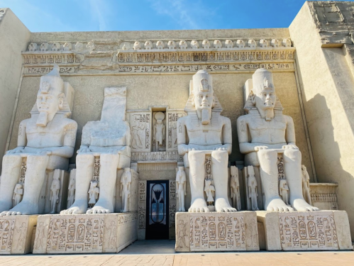 Ancient stone statues of pharaohs flanking a grand entrance, adorned with hieroglyphics and a clear blue sky above.