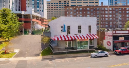 A white building with a red and white striped awning, surrounded by urban structures and parked cars.