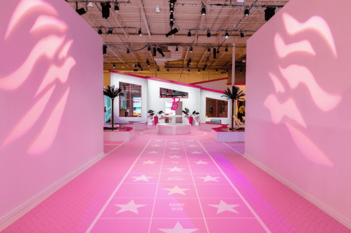 A vibrant pink hallway leading to a stylish, modern space with star patterns and palm trees, themed around Barbie.