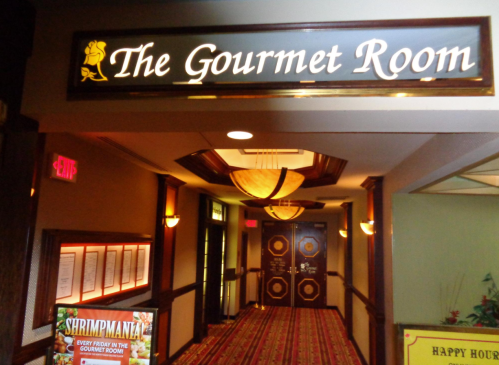 Sign for "The Gourmet Room" with a decorative entrance and menu display in a hallway.