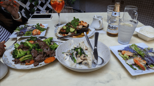 A table set with various dishes, including beef stir-fry, seafood, and a colorful drink, in a cozy dining setting.