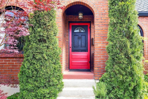 A red door framed by tall green shrubs and brick walls, leading to a welcoming entrance.