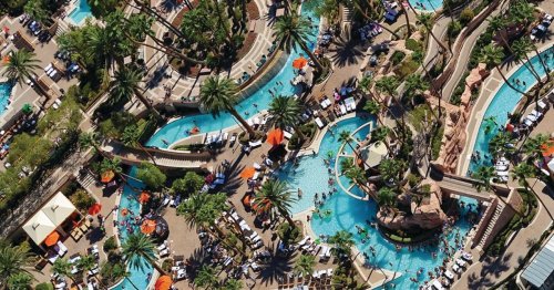 Aerial view of a vibrant resort pool area with winding water features, palm trees, and sun loungers.