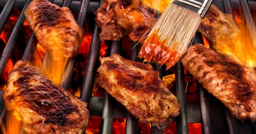 Grilled chicken wings sizzling on a barbecue, with flames and a brush applying sauce.