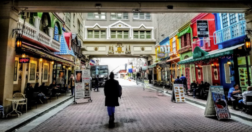A person walks through a colorful alley lined with shops and cafes, with vibrant buildings on either side.