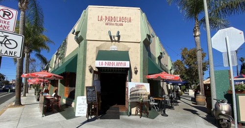 Exterior of La Parolaccia, an Italian restaurant with outdoor seating, palm trees, and a welcoming entrance.