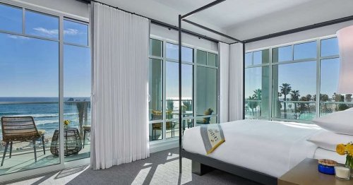 Bright, modern bedroom with a beach view, featuring large windows, a four-poster bed, and stylish decor.