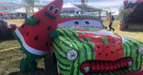 A watermelon-themed car with a character in a watermelon costume, both set in a festive outdoor event.