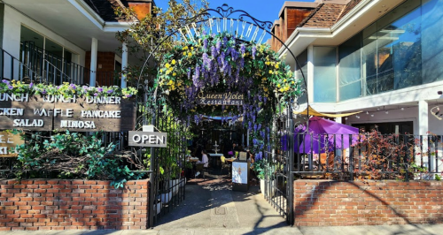 Entrance to Queen Violet Restaurant, adorned with flowers and greenery, featuring an "Open" sign and outdoor seating.