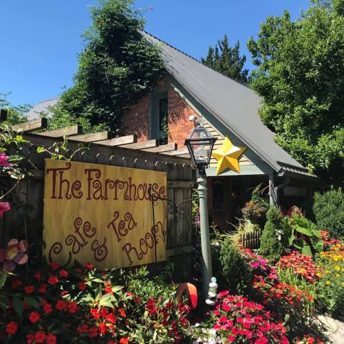 A charming café with a colorful garden, featuring a sign that reads "The Farmhouse Café & Tea Room" and a decorative star.