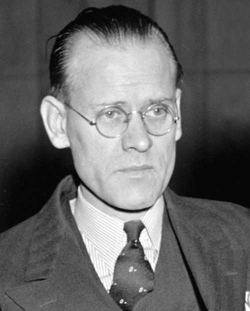 A black and white portrait of a man with glasses, wearing a suit and tie, looking serious and contemplative.