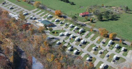 Aerial view of a campground with numerous RVs parked along paved paths, surrounded by green fields and autumn trees.