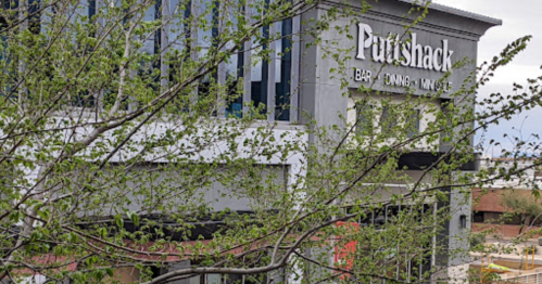 Exterior of Putts Shack, a bar and mini-golf venue, partially obscured by budding tree branches.