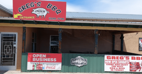 Signage for Greg's BBQ featuring hours, entrance, and "Open for Business" message with Coca-Cola branding.