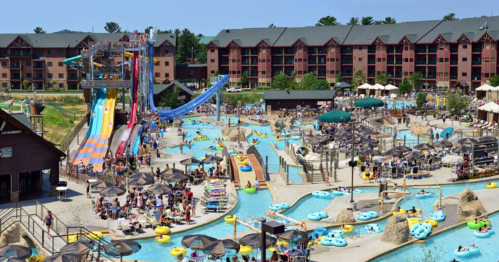 A vibrant water park with slides, pools, and many visitors enjoying a sunny day. Surrounding buildings in the background.