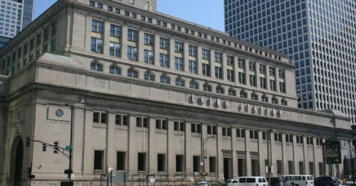 Historic building with a classical facade, surrounded by modern skyscrapers and city streets.