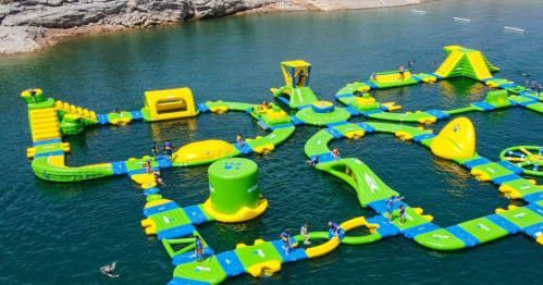A colorful inflatable water park with various slides and obstacles, set on a clear blue lake.