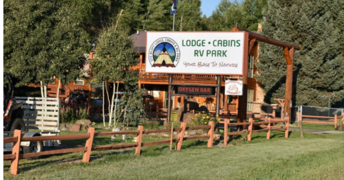 A lodge and cabins RV park with a sign reading "Your Base to Nature" and an "Oxygen Bar" in a green, wooded area.