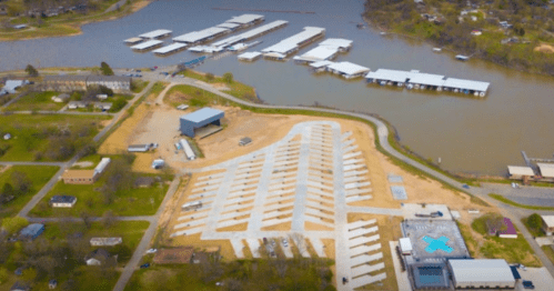 Aerial view of a marina with boat docks, parking areas, and surrounding green spaces near a river.