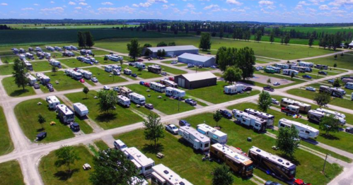 Aerial view of a large RV park with numerous parked RVs and green fields in the background under a blue sky.