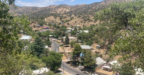 A scenic view of a small town nestled in a valley, surrounded by hills and greenery under a clear blue sky.