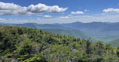 A panoramic view of lush green mountains under a blue sky with fluffy clouds.