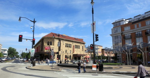 A busy intersection with traffic lights, a historic building, and pedestrians walking on a sunny day.