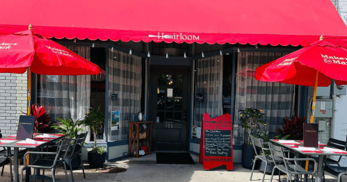 Exterior of a restaurant named "Heirloom," featuring red umbrellas, a welcoming entrance, and outdoor seating.