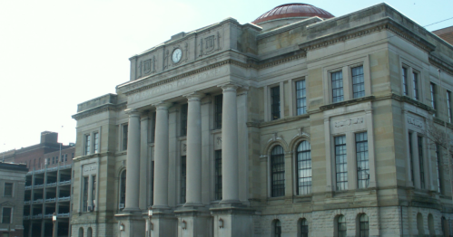 Historic building with large columns, a clock, and a red dome, set against a clear sky.