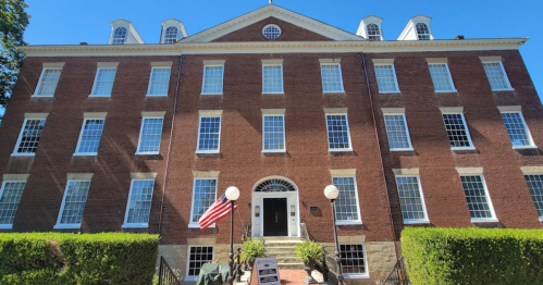 Historic brick building with large windows, an American flag, and a staircase leading to the entrance.