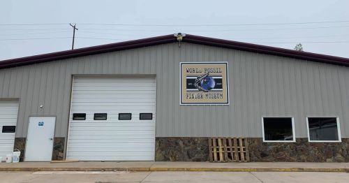 Exterior of the World Fossil Finder Museum, featuring a large sign and a garage door, with a stone foundation.