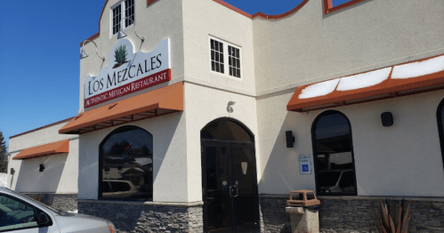 Exterior of Los Mezcales, a Mexican restaurant, featuring a sign, windows, and a stone facade.