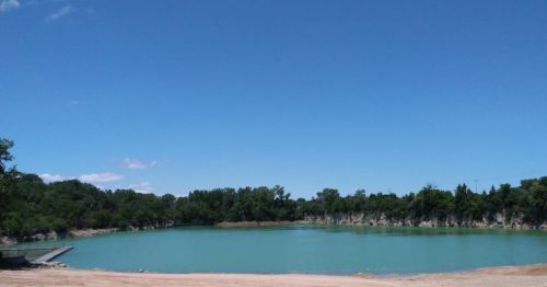 A serene turquoise lake surrounded by green trees under a clear blue sky.